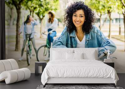 Portrait of young beautiful girl with rental bicycle smile at camera outdoors. Female friends hanging out enjoying summer vacation together outdoors. Travel and people concept. Wall mural