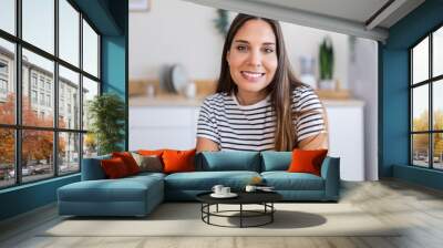 POV of young woman having a video call working from the kitchen at home. She is looking at camera. Business and home office concept. Wall mural