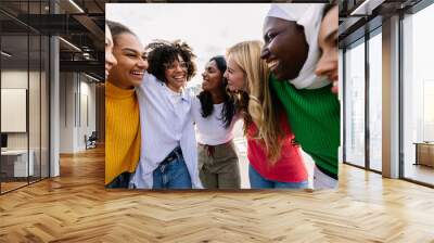 Seven happy young adult women from different cultures laughing together outdoors. Female friendship concept with diverse group of girls friends hugging each other having fun at city street Wall mural