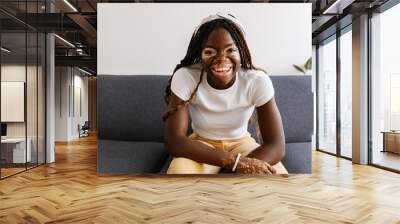 Smiling portrait of young african woman with vitiligo looking at camera sitting on sofa. Diversity, youth and real people concept. Wall mural