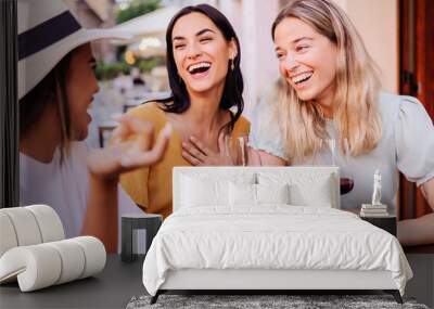 Three happy diverse women having fun enjoying aperitif with red wine sitting at an outside table in a bar. Food and beverage concept. Wall mural