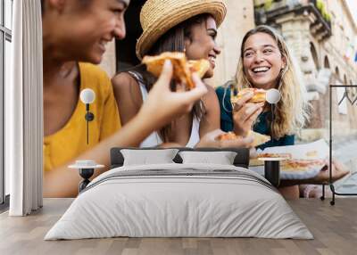 Three young multiracial women laughing while eating a piece of pizza in italian city street - Happy female friends enjoying holidays together in Italy - Friendship, travel and tourism concept Wall mural