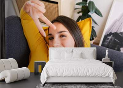 Vertical shot from above of young pretty woman taking selfie portrait lying on sofa at home Wall mural