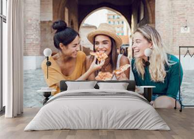 Vertical shot of happy multiracial women eating pizza in city street - Three diverse female tourist having fun on summer holidays in Italy - Friendship and vacation concept Wall mural