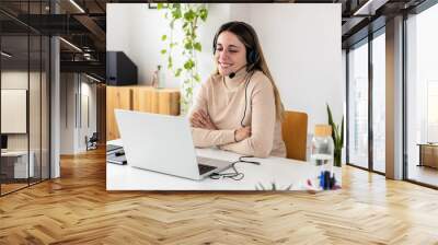 Young adult business woman with headset working on laptop having a video call sitting at home office Wall mural