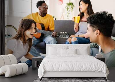 Young diverse friends having fun together at home - International group of teenage people enjoying free time together social gathering and playing the guitar while relaxing at apartment Wall mural