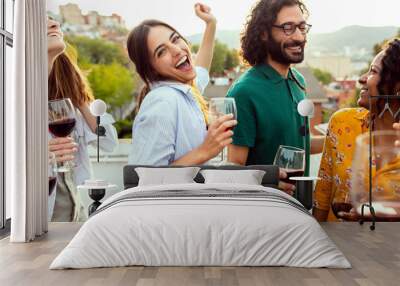 Young group of friends having fun toasting red wine while dancing together at rooftop summer sunset party. Wall mural