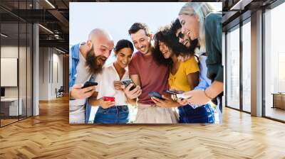 Young group of happy people smiling while using mobile phone together - Smiling multiracial friends standing outdoors in the park holding cellphone - Technology, youth and social media concept Wall mural