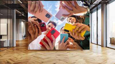 Young group of people using mobile phone device standing together in circle outdoors. Millennial friends addicted to social media app, betting or playing video game on platform online. Wall mural