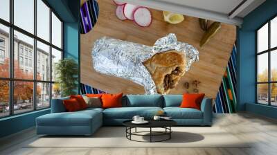 Burrito wrapped in foil surrounded by peppers, radishes, and lime - overhead Wall mural