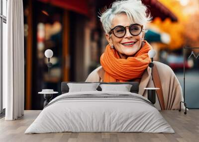 A positive, cheerful older woman walks along the streets of an autumn city with a paper cup of a hot coffee drink Wall mural