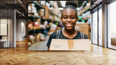 Joyful young girl, dark skinned teenager, volunteer in warehouse, carrying box with groceries in community food bank, volunteer center Wall mural