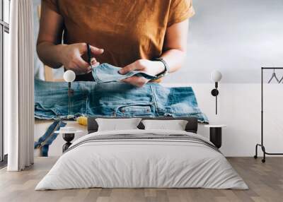 Woman repairs sews reuses fabric from old denim clothes economical reuse Wall mural