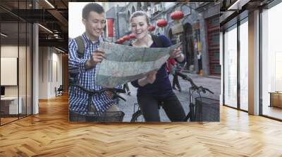 Young man and woman on bicycles, looking at map. Wall mural