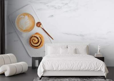 Freshly baked cinnamon bun with spices and cocoa filling and coffee or cappuccino with latte art on white serving plate over white marble background. Top view. Copy space for text. Swedish breakfast. Wall mural