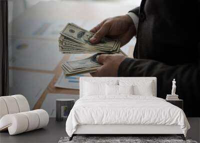 Young asian businessman standing count a dollar bill from his desk. The concept of business results. Wall mural