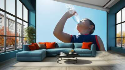 Little asian boy drinking water against blue sky Wall mural