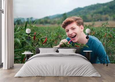 Young European teenager in a field of thai red and green chilies with mouth open eating it. traveling visiting countries for agriculture, outdoor nature and countryside farm mountain background. Wall mural