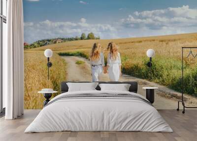 Two girls walk in countryside road.  Outdoor photo of twins sisters posing on nature background. Summer vacation in countryside. Back view. Wall mural