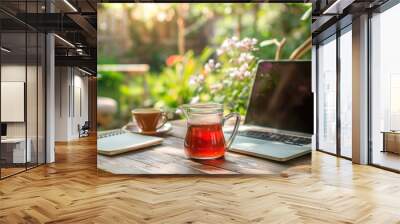 A serene setting for remote work with a laptop and a hot beverage on a wooden table surrounded by lush plants and morning sunlight. Wall mural