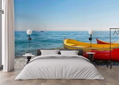 Red and yellow sailing boats resting on the bank of a sunlit sea, with clear blue summer skies and gentle waves lapping at the shore. Wall mural