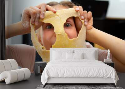 Adorable girl covering face with mask of dough Wall mural