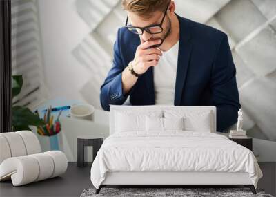 Busy man sitting at desktop and holding papers in hand. He is checking them carefully and precisely   Wall mural