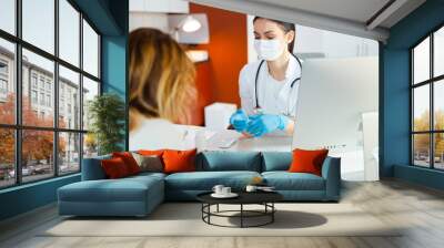 Caucasian doctor in medical mask talking to female patient Wall mural