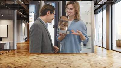 Cheerful male in eyeglasses watching at reflection while standing opposite female. Client in optician store concept Wall mural