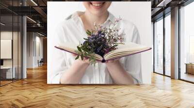 Cheerful young woman holding open book with flowers Wall mural