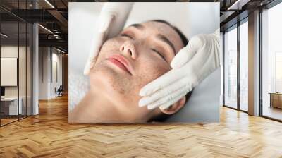 Close up of asian girl enjoying skin care treatment. Beautician hands pampering her face with scrub Wall mural