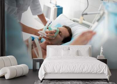 Close up of unconscious middle aged man getting mechanical ventilation in hospital and female hands using respiratory equipment Wall mural