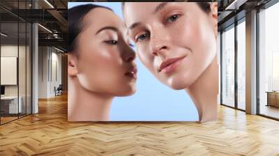 Close up portrait of attractive interracial women situating against blue background Wall mural