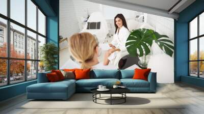 Day at wellness center. Portrait of beautiful lady in white bathrobe sitting in armchair and looking at master with smile Wall mural