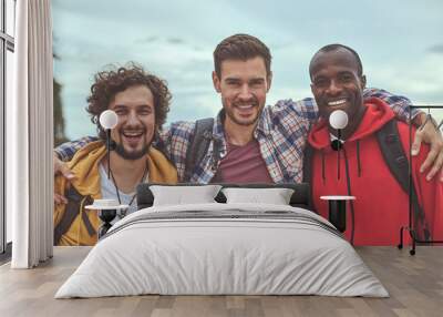 Diverse but together. Waist up portrait of positive guys making friendly embrace and smiling in front of camera Wall mural