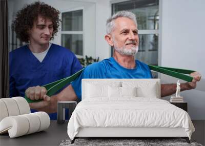 Elderly man using fitness rubber band in his hands during rehabilitation with his young coach Wall mural