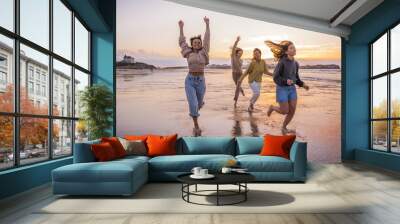 Full length view of the four young female friends running through the sea shore, laughing and jumping Wall mural