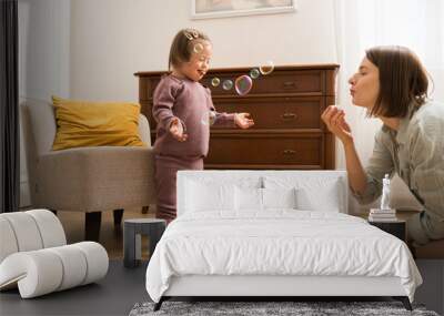 Girl with down syndrome feeling fun while her young mother blowing soap bubbles Wall mural