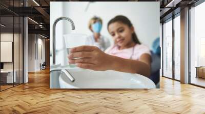 Grinning young girl is holding glass with water at dentist Wall mural