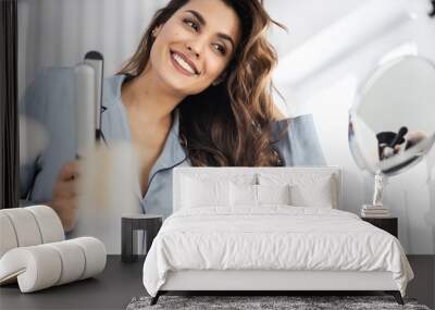 Happy pretty woman holding curling iron at home Wall mural