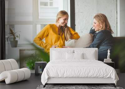 I am happy for you. Cheerful woman is touching belly of her pregnant friend. They are sitting on sofa and smiling  Wall mural