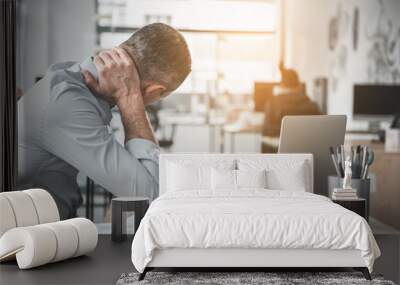 Man holding sore neck while using notebook computer. He sitting at table. Sick worker concept Wall mural