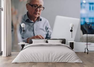 Old man in glasses using modern white laptop Wall mural