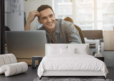 Portrait of cheerful man typing in laptop while sitting at desk in office. Beaming employee at job concept Wall mural