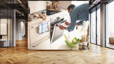 Portrait of gentleman in denim shirt closing door of oven while looking at frying pan with beef steak Wall mural