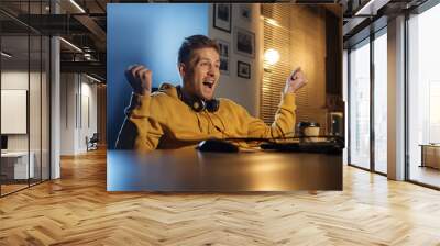 Portrait of happy man gesturing hands while sitting at table. He looking at computer. Win concept Wall mural