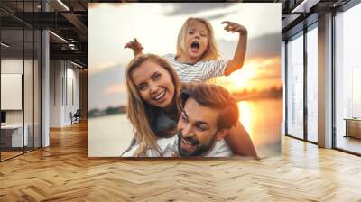 portrait of happy unshaven husband spending tie with cheerful wife and satisfied female child in nat Wall mural