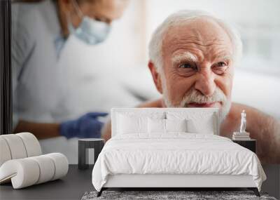 Portrait of shirtless bearded gentleman feeling pain during injection. Female doctor in protective mask on blurred background Wall mural