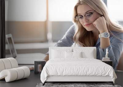 Portrait of successful young businesswoman reading document with concentration. She is sitting at desk in office Wall mural