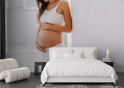 Pretty young woman holding hands on belly and looking down Wall mural